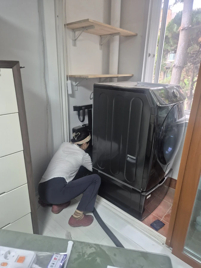 다용도실 세탁건조기 뒤편을 몸을 굽혀 확인하는 작업자 — 배수구 청소 관련 거주청소 현장사진