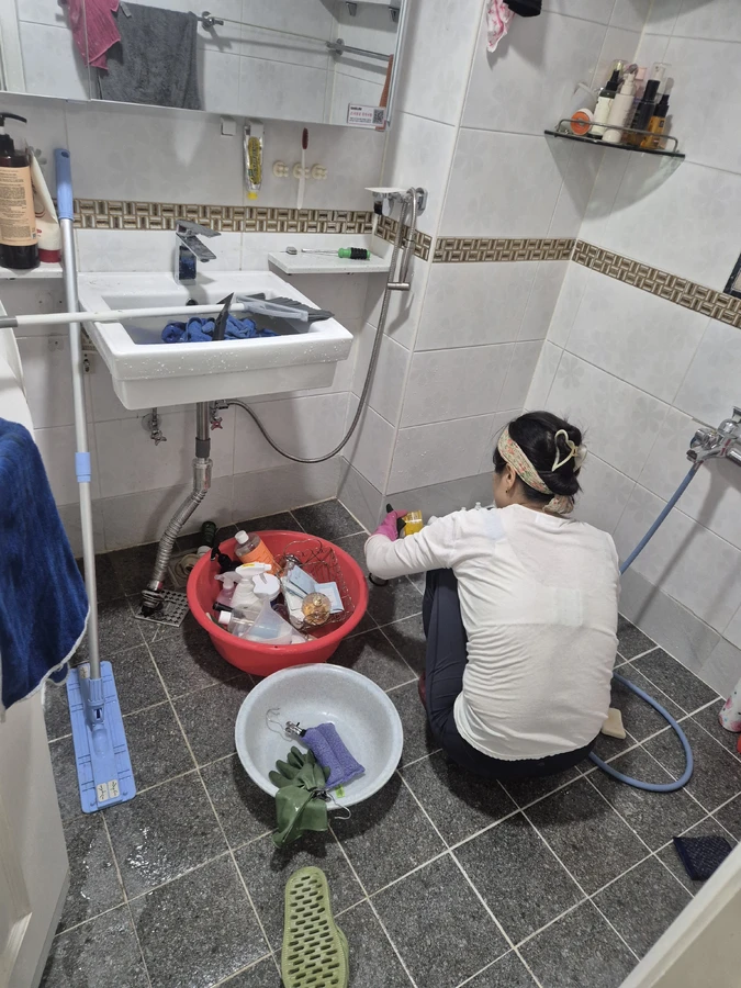 세면대 아래에 앉아 욕실 바닥을 닦는 작업자